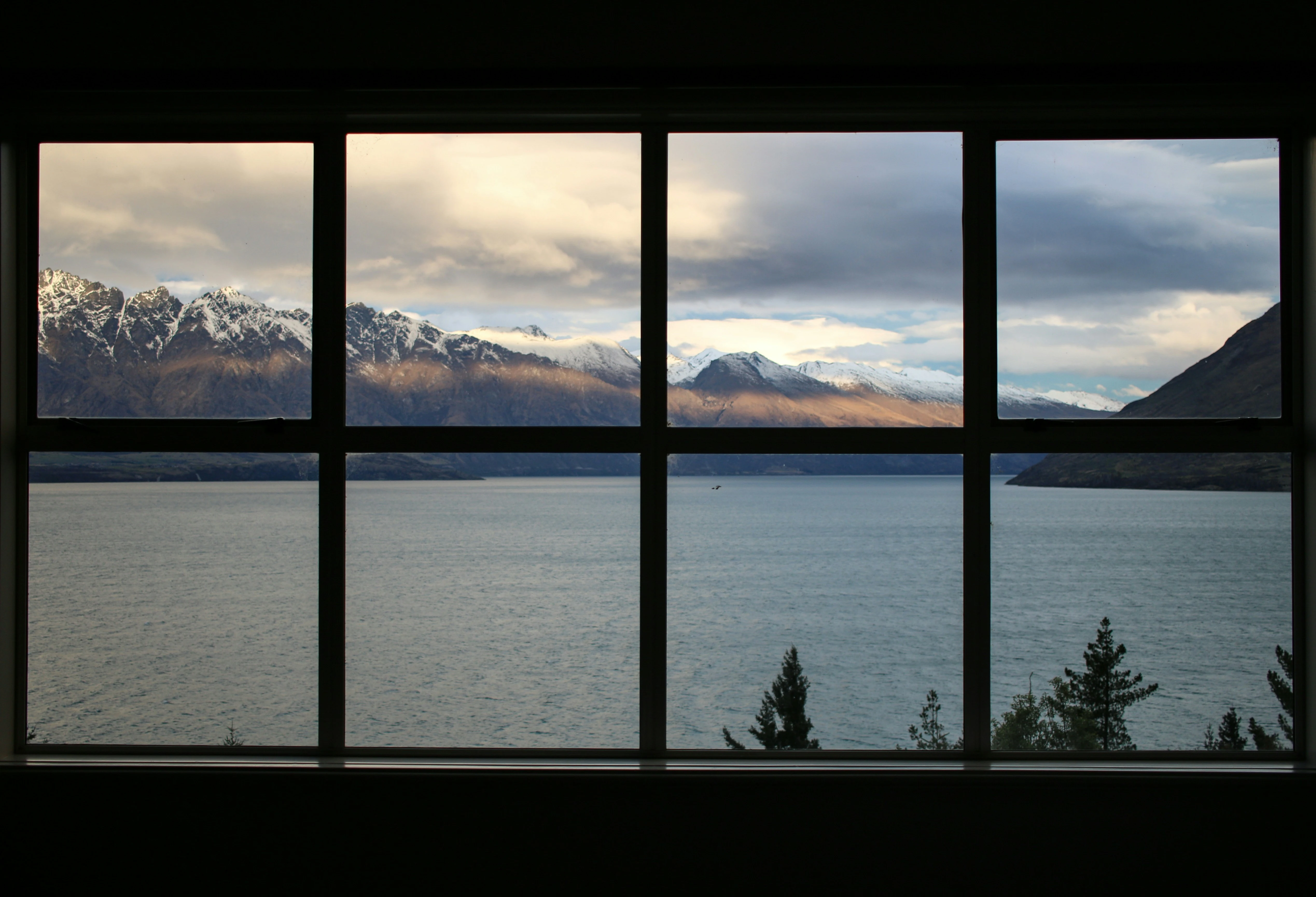 Calm body of water near a brown mountain under a white and gray sky